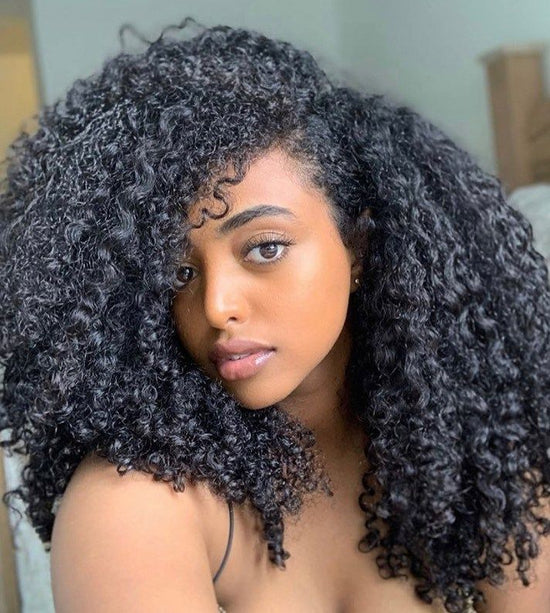 Woman with voluminous curly hair, wearing a black top, gazing at the camera.